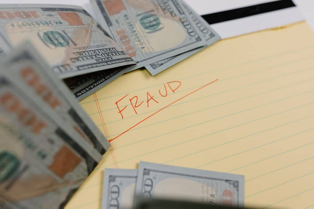 A photo that shows the word "FRAUD" handwritten on a yellow notepad with hundred dollar bills scattered around. Crossroads Investigations does fraud investigations in Florida.