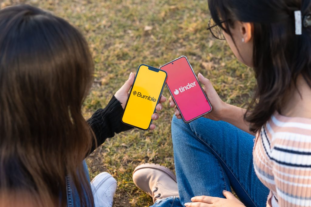A photo of two adolescents looking at their smartphones with the dating apps Bumble and Tinder.